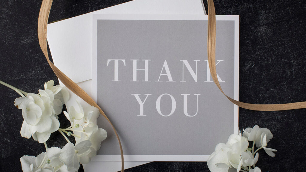 Elegant gray and white thank you note on a slate black table top from above