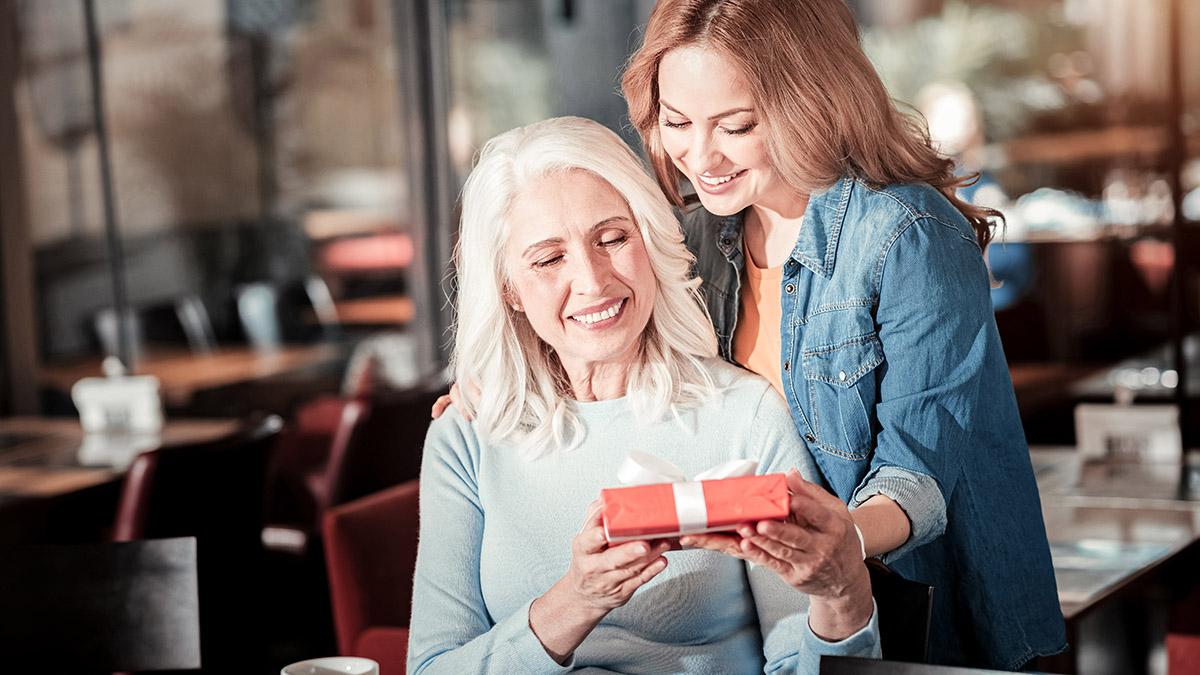 Positive aged woman getting a lovely present from her attentive granddaughter